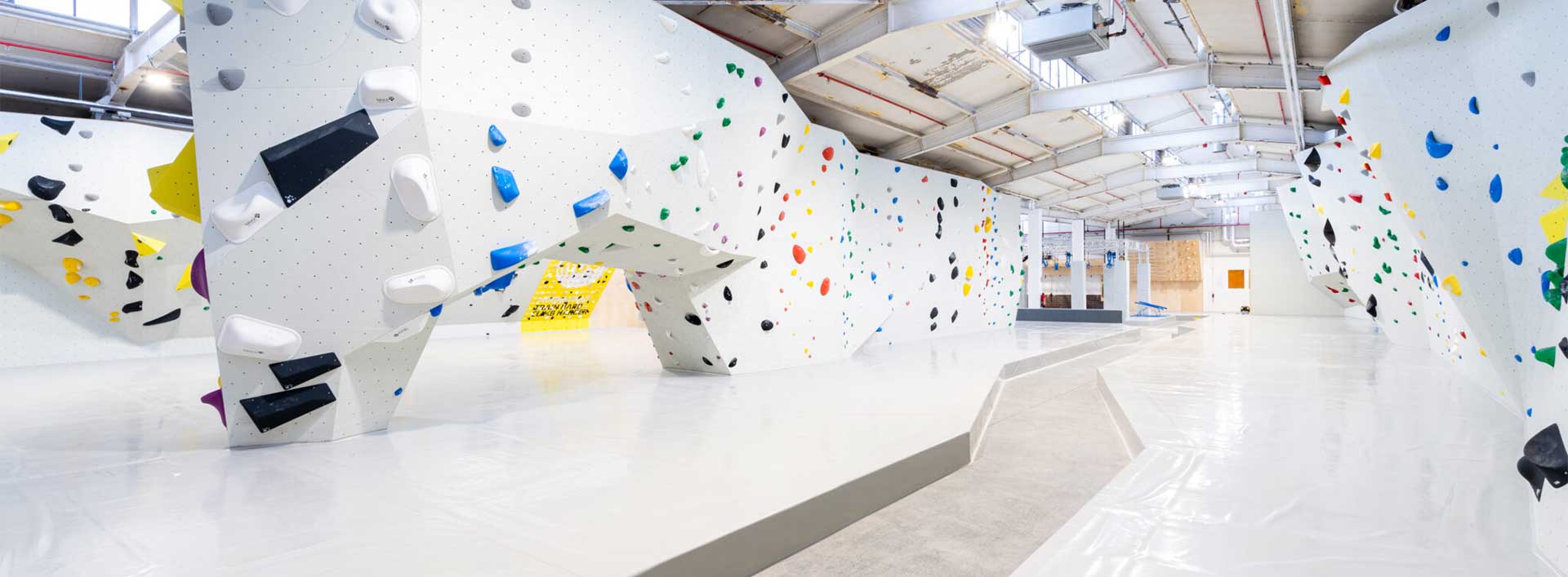 Eine Überhang Boulderwand mit weißen Wänden sowie Fallschutzmatten und bunten Griffen, von 3D Sportanlagen designt und gebaut.